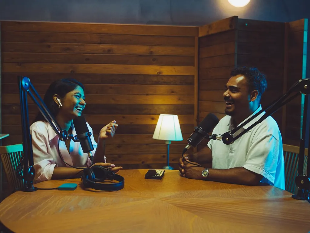 Two podcast hosts laughing at their microphones